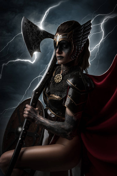 Portrait of violent goddes dressed in armor holding axe against heaven and thunderstorm. - Fotó, kép