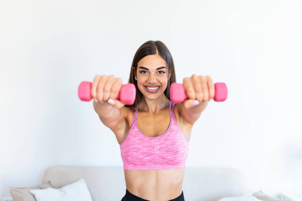 Woman exercising with dumbbells at home. Sporty beautiful woman exercising at home to stay fit. Young woman exercising at home in a living room. Fitness, workout, healthy living and diet concept. - Fotoğraf, Görsel
