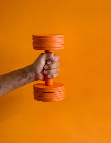 photo of a dumbbell in a strong male hand orange background - Fotografie, Obrázek