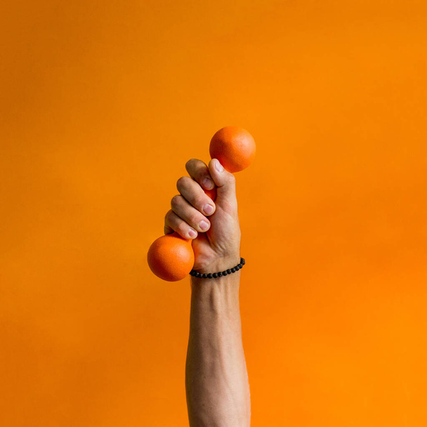 photo of an orange small dumbbell in a male hand background orange - Foto, Bild
