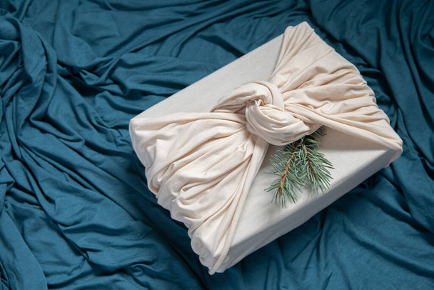 Christmas, New Year present in ivory fabric on deep blue background. Trendy zero waste gift wrapping. Sustainable design concept. - 写真・画像