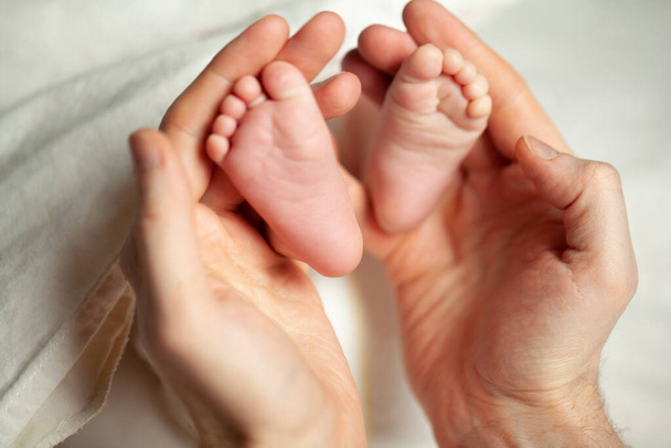 Erkek avuçlarında bebeğin ayakları birbirine yakın. - Fotoğraf, Görsel