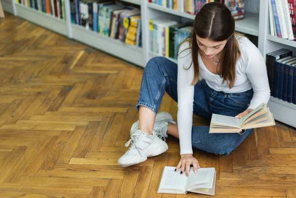 high angle view of teenage girl with books sitting on floor in library - Fotoğraf, Görsel