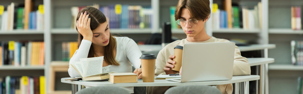 парень в очках держит кофе, чтобы подойти к ноутбуку и девушка-подросток в библиотеке, баннер - Фото, изображение
