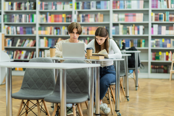 teenage students studying near laptop and books in library  - Valokuva, kuva