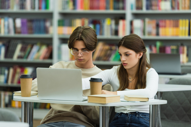 teenage girl and guy in eyeglasses studying near laptop and books in library - Fotografie, Obrázek