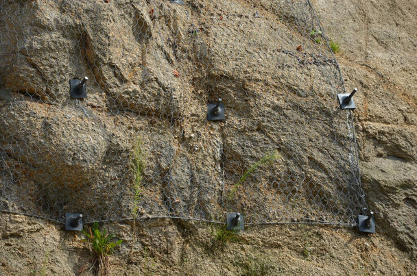 οπλισμένη κλίση με χαλύβδινο δίχτυ αγκυρωμένο βαθιά μέσα σε βράχο. Οι πέτρες που πέφτουν δεν πέφτουν στο δρόμο. αγκυροβολημένο με ατσάλινα καρφιά. διάτρηση στο υπέδαφος και στερέωση του ματιού, σιδηροτροχιά - Φωτογραφία, εικόνα