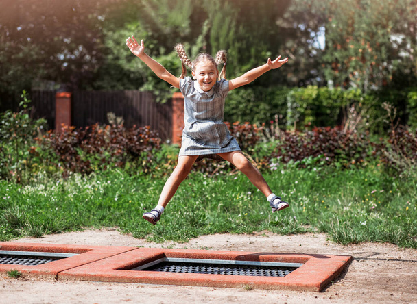 Маленькая девочка прыгает на батуте в парке. Счастливый смеющийся ребенок на открытом воздухе во дворе на летних каникулах. Прыгай выше  - Фото, изображение