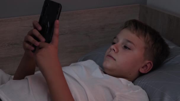 Мужчина-подросток лежит на кровати, просматривая соцсети на телефоне. Проблемы подростков, зависимость от социальных сетей - Кадры, видео