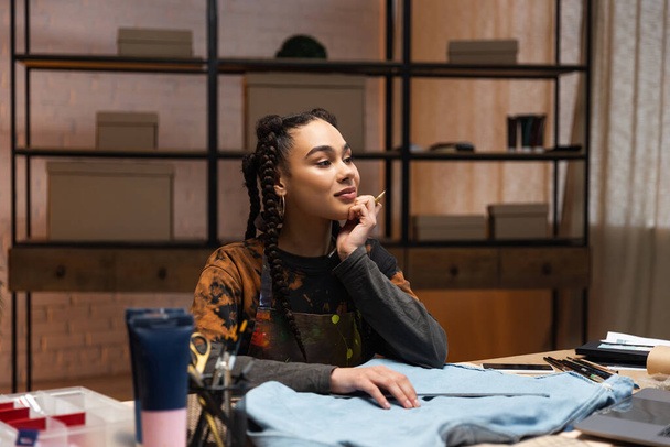 Африканский американский дизайнер сидит рядом с тканями и швейным оборудованием в мастерской  - Фото, изображение