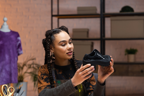 Smiling african american designer holding shoe in workshop  - Foto, afbeelding