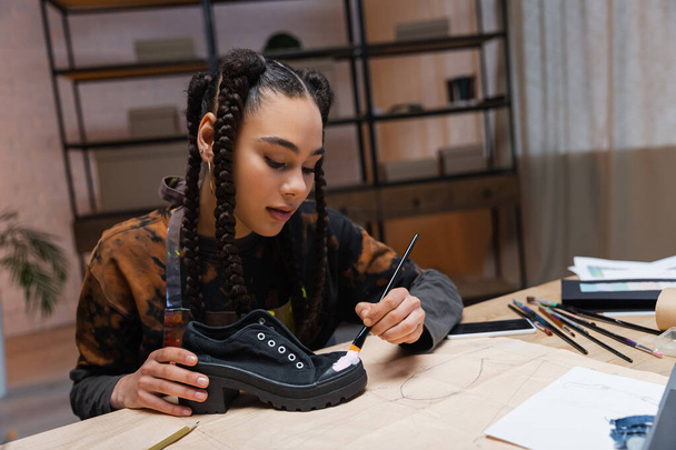African american craftswoman painting on shoe near sketch and sewing pattern  - 写真・画像