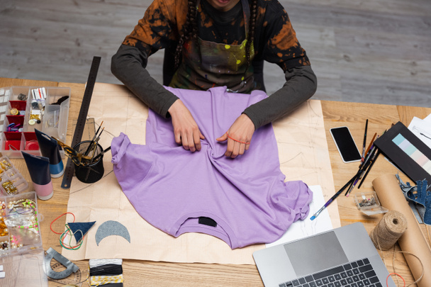 Cropped view of african american craftswoman working with t-shirt in workshop  - Foto, Bild