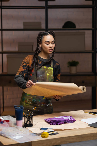 African american craftswoman holding craft paper near cloth in workshop  - Foto, Imagen