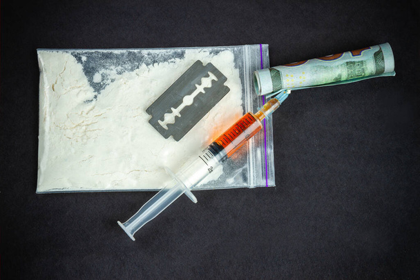 Top view accessories for drug use on black background. Syringe with razor and snorting tube made of money. - Foto, immagini