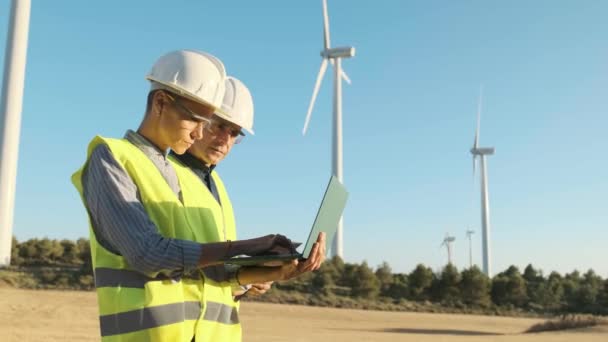 Two engineers using a laptop while working together at a wind turbine field. Sustainable lifestyles, renewable energy and technology concept. - Filmagem, Vídeo