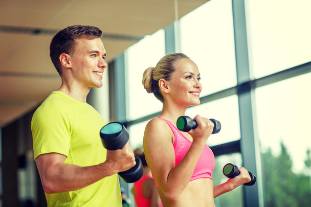 smiling man and woman with dumbbells in gym - Foto, imagen