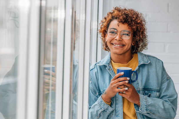 donna afroamericana che sorride alla finestra con una tazza di caffè - Foto, immagini