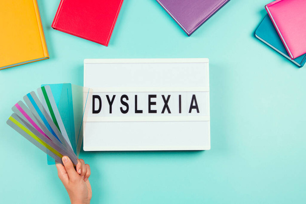 Dyslexia awareness, help children with reading, learning difficulties concept. Lightbox with DYSLEXIA word and kid hand holding reading highlight bookmark overlays lines strips. Top view. - Foto, imagen
