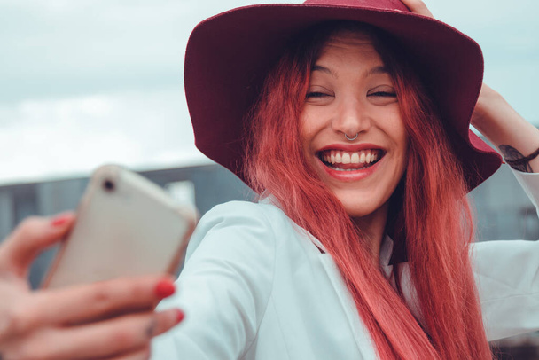 vörös hajú lány vagy fiatal nő kalapban felvétel vagy fotózás mobiltelefonnal - Fotó, kép