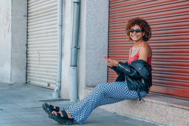 urban stijl zwart latin meisje met mobiele telefoon in de straat - Foto, afbeelding