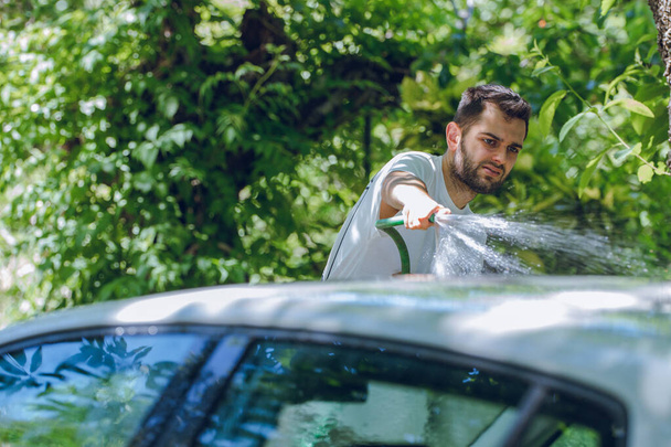 fiatal férfi nyáron mossa az autót tömlővel - Fotó, kép