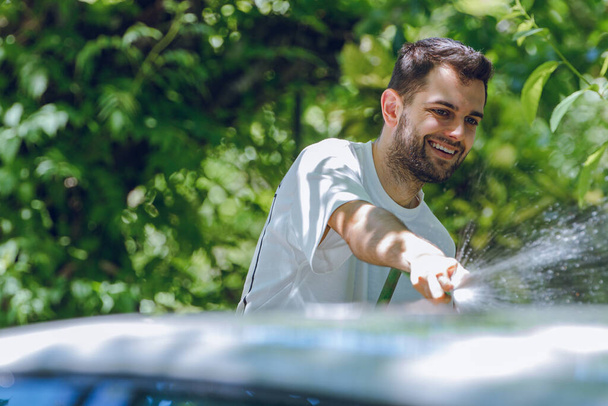 young man in summer washing the car with hose - Foto, afbeelding