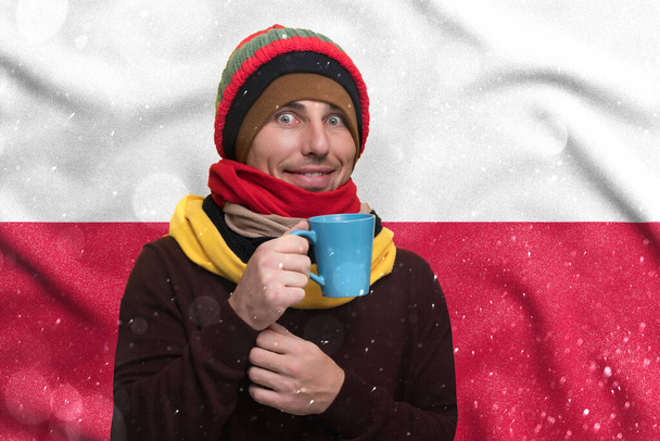 Газовый кризис в Польше, холодная зима и высокие тарифы на газ, улыбающийся мужчина согревается чашкой чая и теплой одеждой. - Фото, изображение