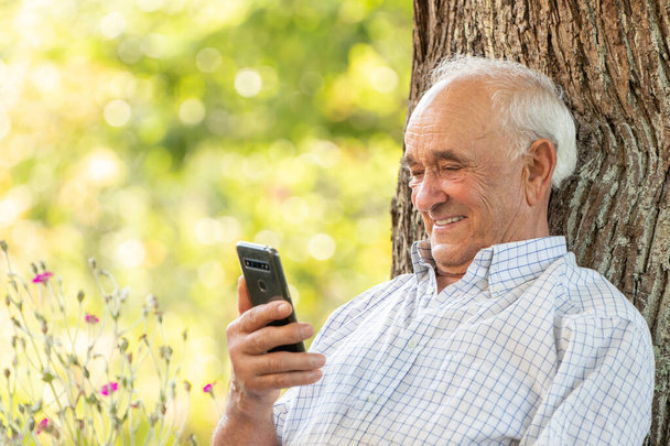 старший чоловік дивиться на мобільний телефон або смартфон, посміхаючись на відкритому повітрі
 - Фото, зображення