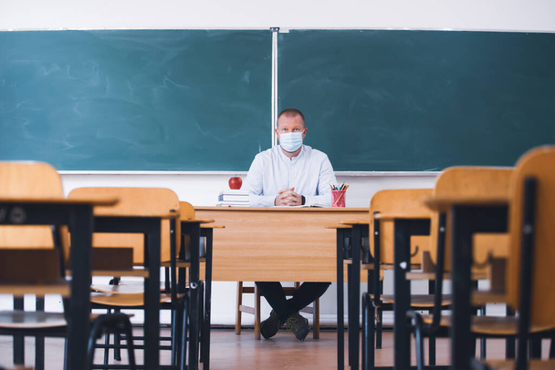Lehrer mit Maske im Klassenzimmer. Soziale Distanzierung und Sicherheit im Klassenzimmer während der Coronavirus-Epidemie - Foto, Bild