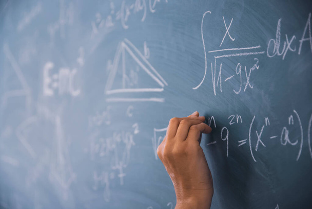 Zbliżenie ręki trzymającej kredę i piszącej równania matematyczne na tablicy. Koncepcja edukacji. - Zdjęcie, obraz