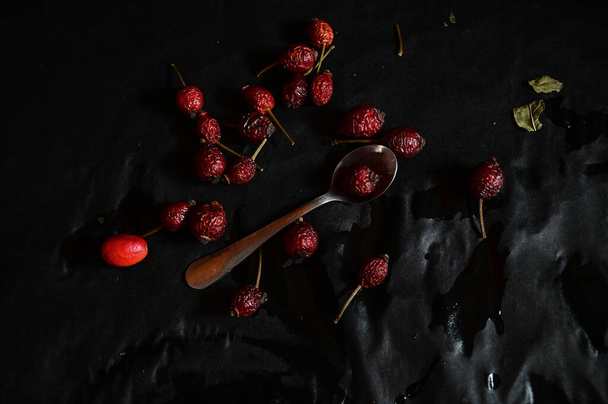 rosehip fruit lying on a teaspoon on a black background, top view - Foto, Bild