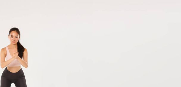 Повна довжина орієнтованого доброзичливого жіночого атлета, азіатська фітнес-дівчина виконує присідання з затиснутими руками і опір розтягування смуги на стегнах, використовуючи тренувальне обладнання під час тренування
. - Фото, зображення
