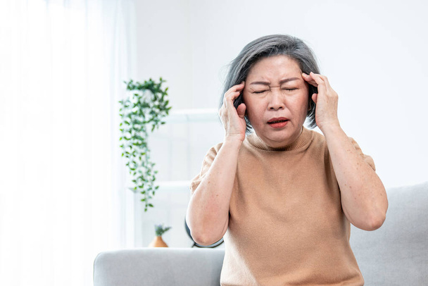 An agonizing senior woman with a headache, compress her temple with both hands at her contented living room. Senior health, nursing home, caretaker service. - Foto, Bild