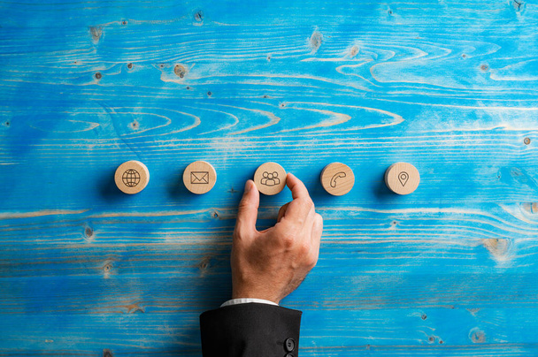 Hand of a businessman placing five wooden cut circles with contact and communication icons on them in a row over textured blue wooden background. - Zdjęcie, obraz