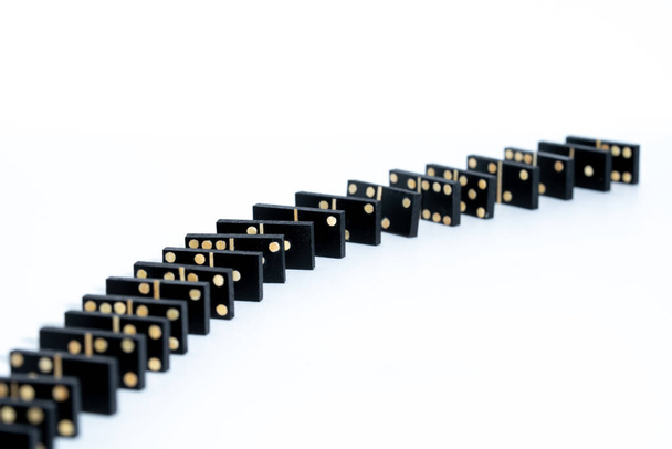 several black domino game tiles, forming a row. the row is viewed from the side, where the domino effect can be seen. they are on a white table. - Foto, afbeelding
