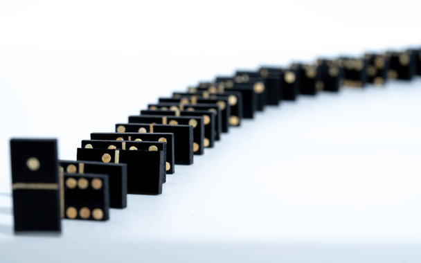 several black domino game tiles, forming a row. the row is viewed from the side, where the domino effect can be seen. they are on a white table - Foto, Imagem