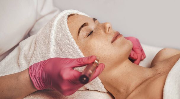 Professional beautician using derma pen on womans face skin, at spa salon. Cosmetology and professional skin care. Girl enjoying skin rejuvenation procedure - Valokuva, kuva