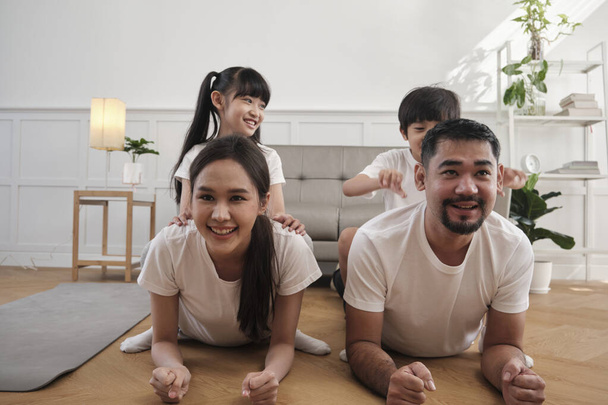 Happy well-being Asian Thai family, children play and tease their parents while yoga fitness training and health exercise together in the white living room, domestic home lifestyle, weekend activity. - Foto, Imagem