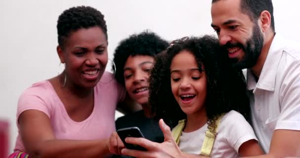 Międzyrasowa rodzina i dzieci śmieją się razem patrząc na komórkę w domowej sofie - Materiał filmowy, wideo