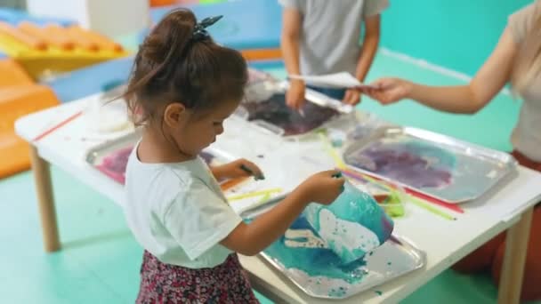 Multicultural group of children at the nursery school. Ethnic little girl milk painting, using pigments for color. Finger paint. High quality 4k footage - Filmmaterial, Video