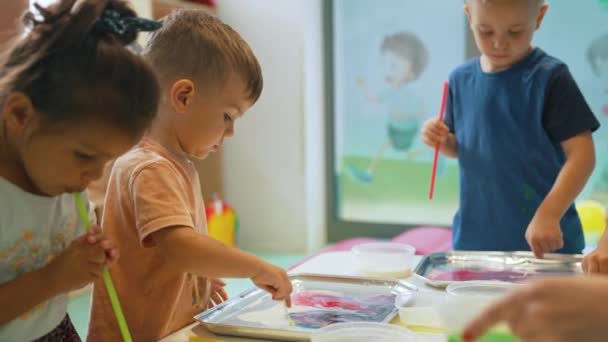 Багатоетнічна група малюків молочного живопису з вчителем допомагає їм, використовуючи харчові барвники для кольорів. Дитячий малюнок пальців на уроках дитячої школи. Високоякісні 4k кадри
 - Кадри, відео