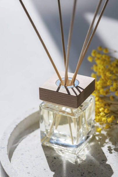 Transparent bottle of aroma diffuser on the terazzo podium on white background. Eau de parfum for home presentation on a podium with field flowers. Trending concept in natural materials. - Foto, afbeelding