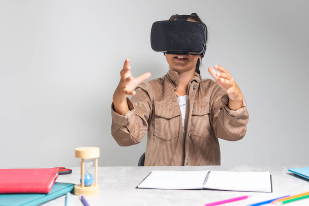 Küçük çocuk, VR gözlükleriyle ödev yapıyor ve masada online dersler veriyor. Kulaklıklı genç bir kız okulda uzak kurslara ve evde derslere hazırlanıyor. Teknolojili liseli kız - Fotoğraf, Görsel