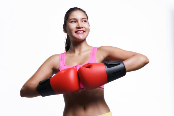 Asiatin mit Boxhandschuhen im Fitness-Outfit, während sie aufblickt und auf weißem Hintergrund lächelt. - Foto, Bild