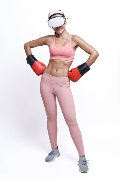 Kobieta pozowała w rękawiczkach bokserskich w stroju fitness i nosiła zestaw słuchawkowy VR na białym tle. - Zdjęcie, obraz