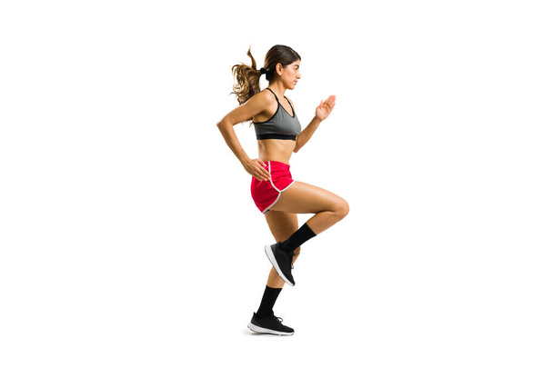 Active hispanic woman wearing sportswear running and doing a cardio workout against a white background with copy space - Foto, Imagen