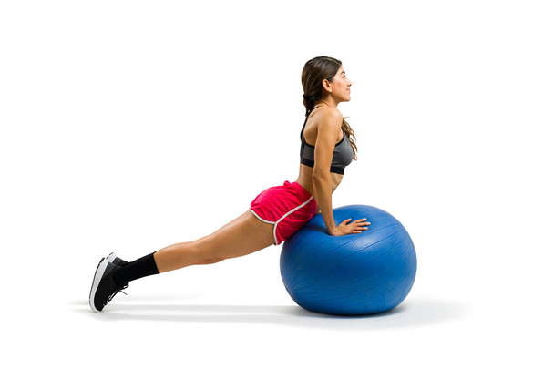 Ευτυχισμένη όμορφη γυναίκα απολαμβάνοντας προπόνηση της και να κάνει μια σανίδα με μια μπάλα σταθερότητας κατά την άσκηση - Φωτογραφία, εικόνα