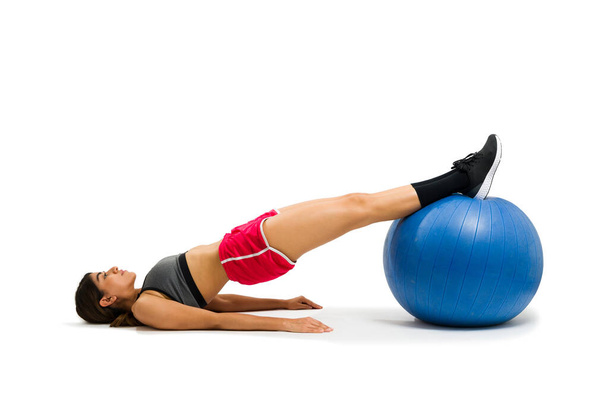 Fit sporty woman on a bridge pose exercise with a stability ball during her cardio workout cut out on a white background - Foto, imagen