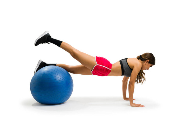 Ισχυρή νεαρή γυναίκα με τρόπο ζωής γυμναστικής κάνει μια σανίδα και μίζες χρησιμοποιώντας μια μπάλα σταθερότητας για την άσκηση καρδιο της - Φωτογραφία, εικόνα